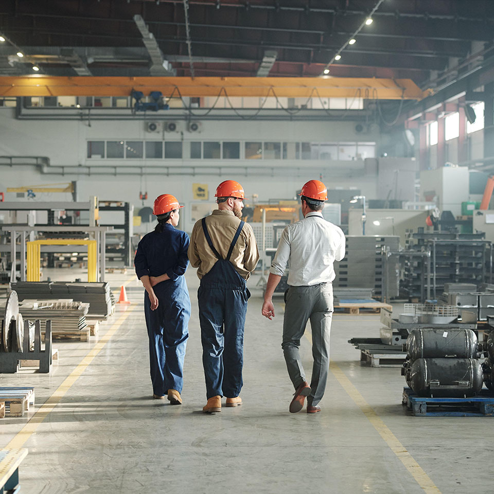 2B12BP1 - Back view of three workers of industrial plant walking along large factory