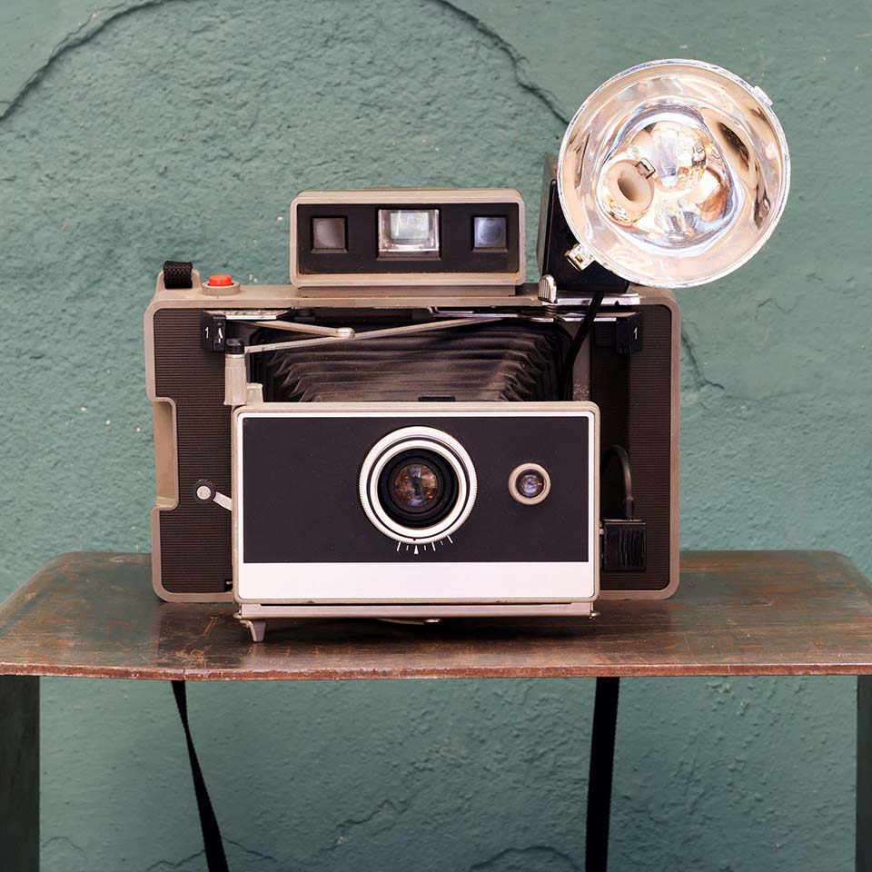 2C97CMM - Old vintage instant camera with bellows and lamp on a small shelf in front of a damaged green textured wall in a photographic concept 