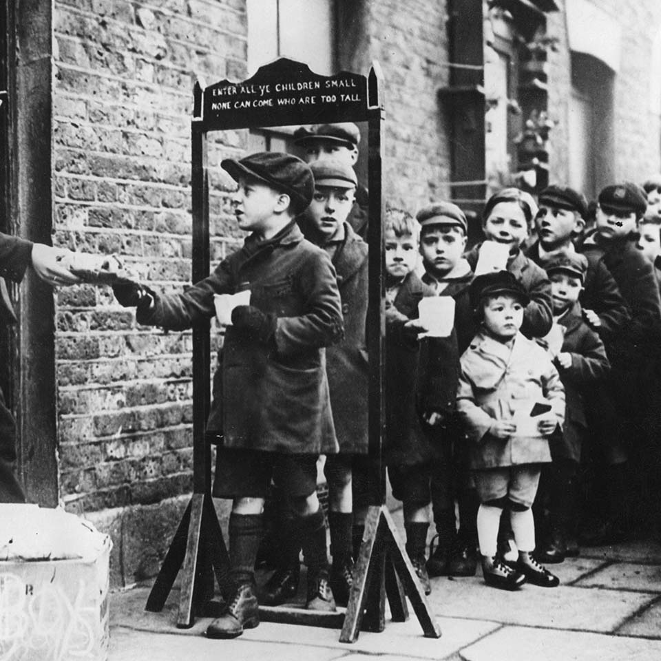 2DBHTBR - "Children in London's East End are queuing up for the distribution of small gift packages from a charity organization. A display measures the maximum allowed size of the children: ""Enter all ye children small none can come who are too tall"".