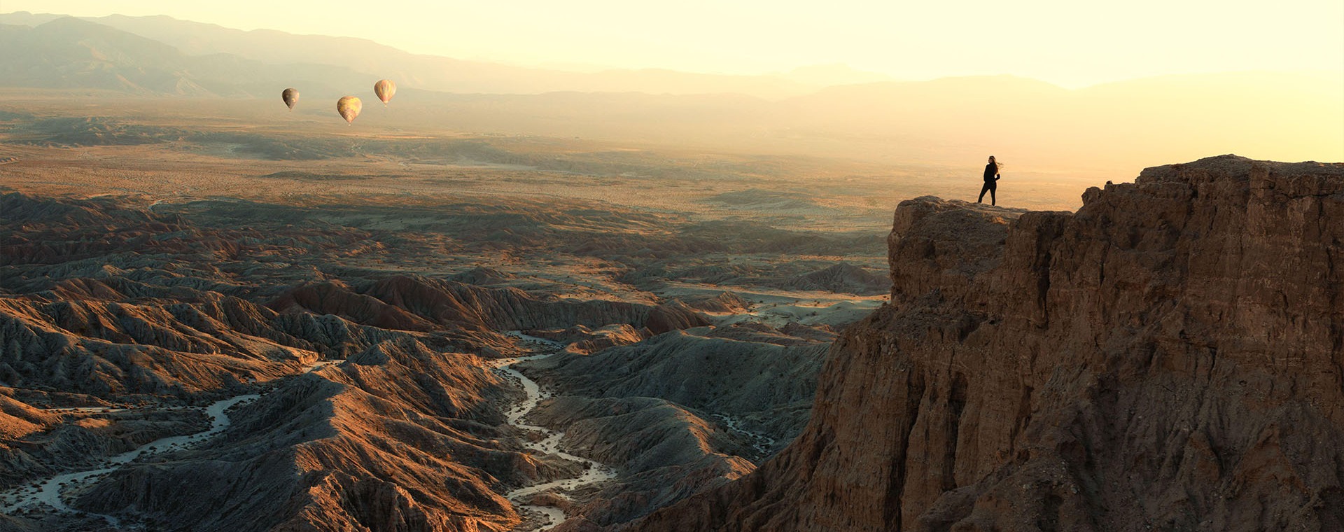 Woman standing on Font's Point looking at hot air balloons flying over badlands, Anza-Borrego Desert State Park, California, USA 