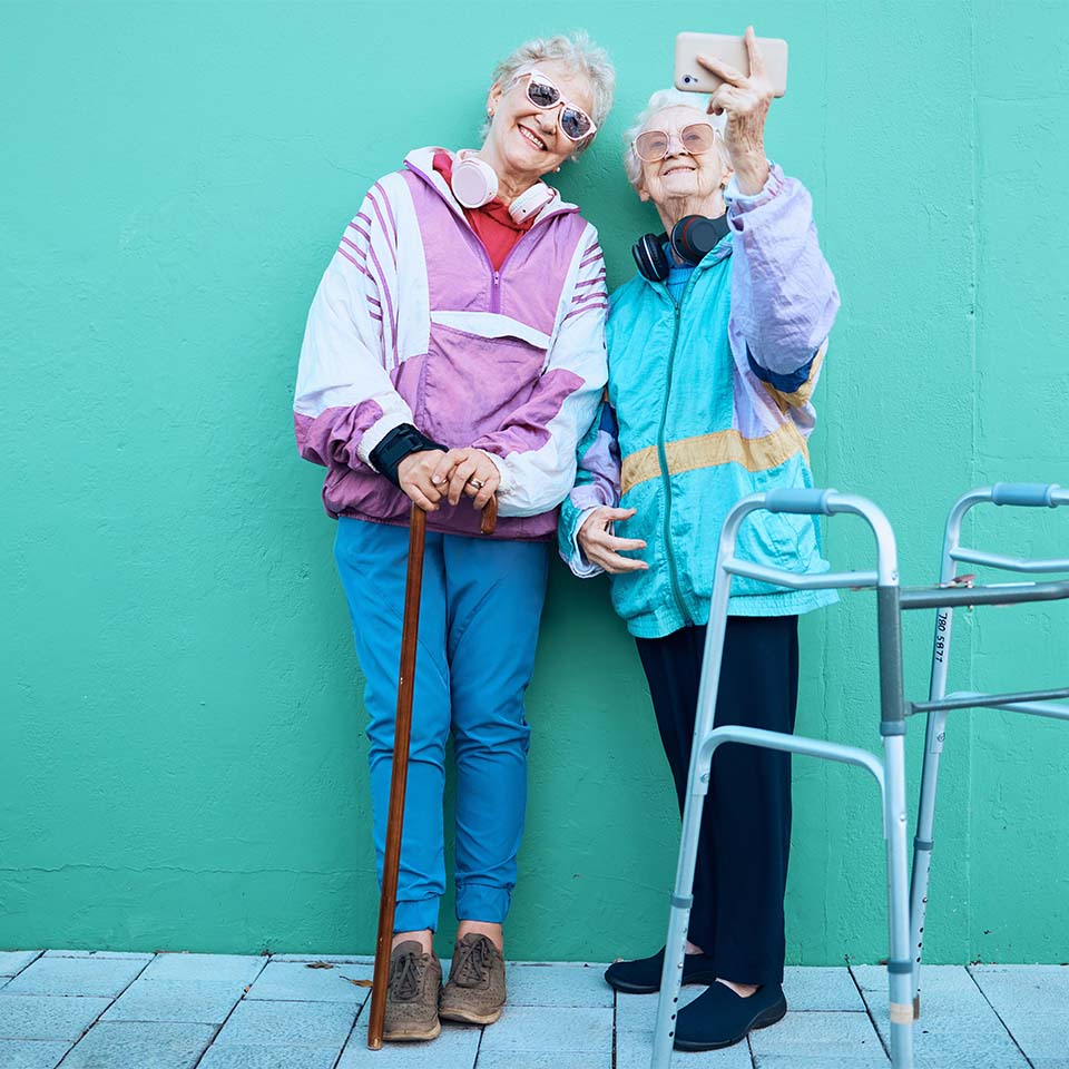  Phone, selfie and disability with senior friends posing for a photograph outdoor on a green wall background. Happy, mobile and walker with a mature 