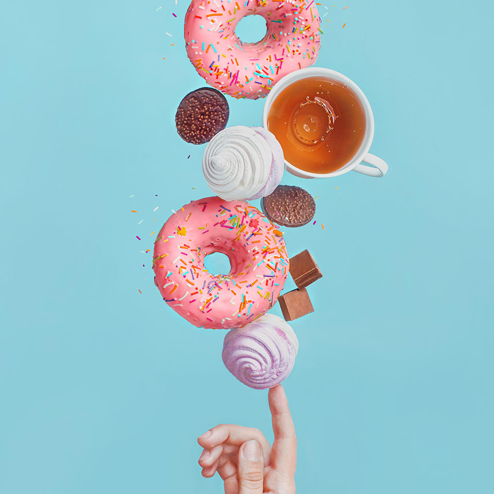 Balancing donuts. Glazed donuts, tea cups, marshmallows and chocolate chips, balancing on the tip of one's finger 