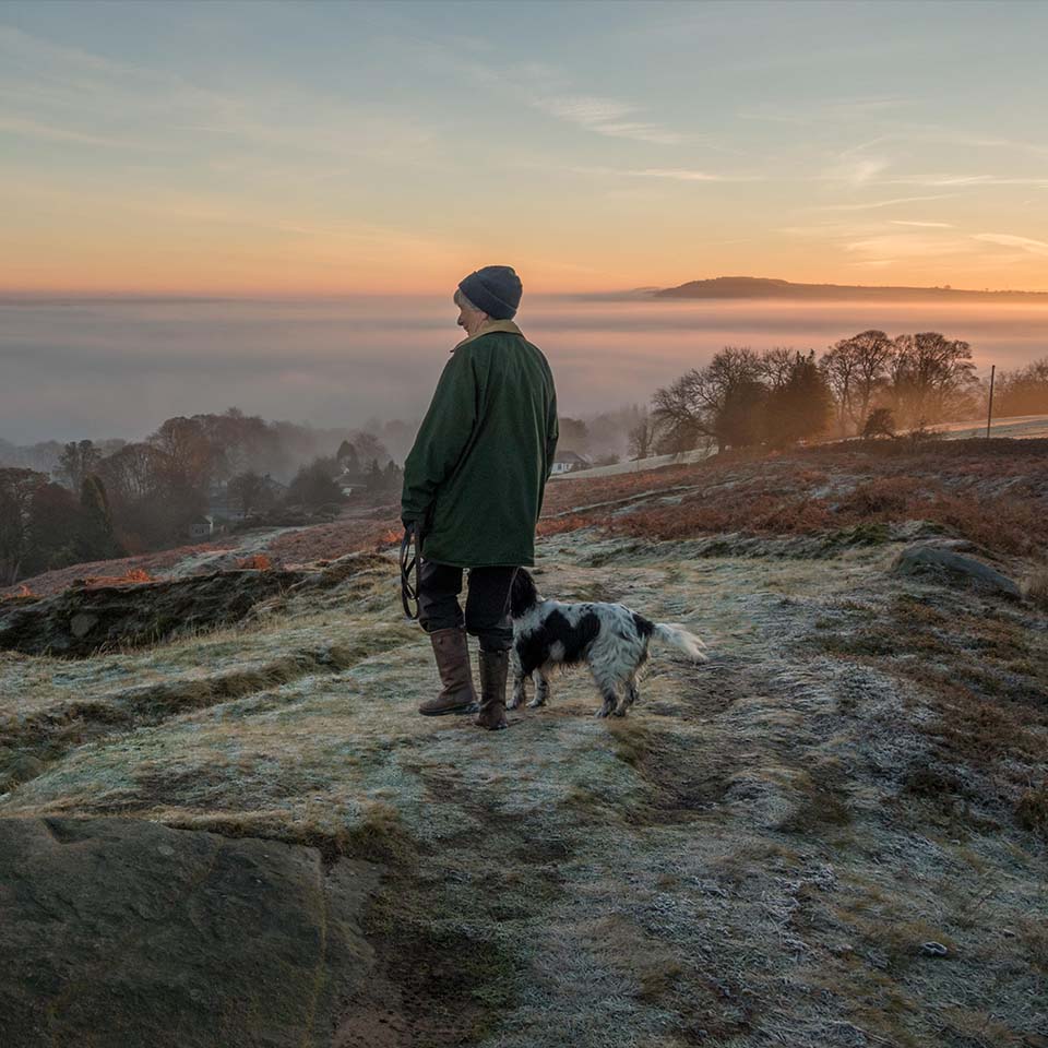 J67671 - woman walking dog on a path on Ilkley Moor on a frosty early morning looking at countryside views of a cloud inversion, Wharfe valley, Yorkshire, UK