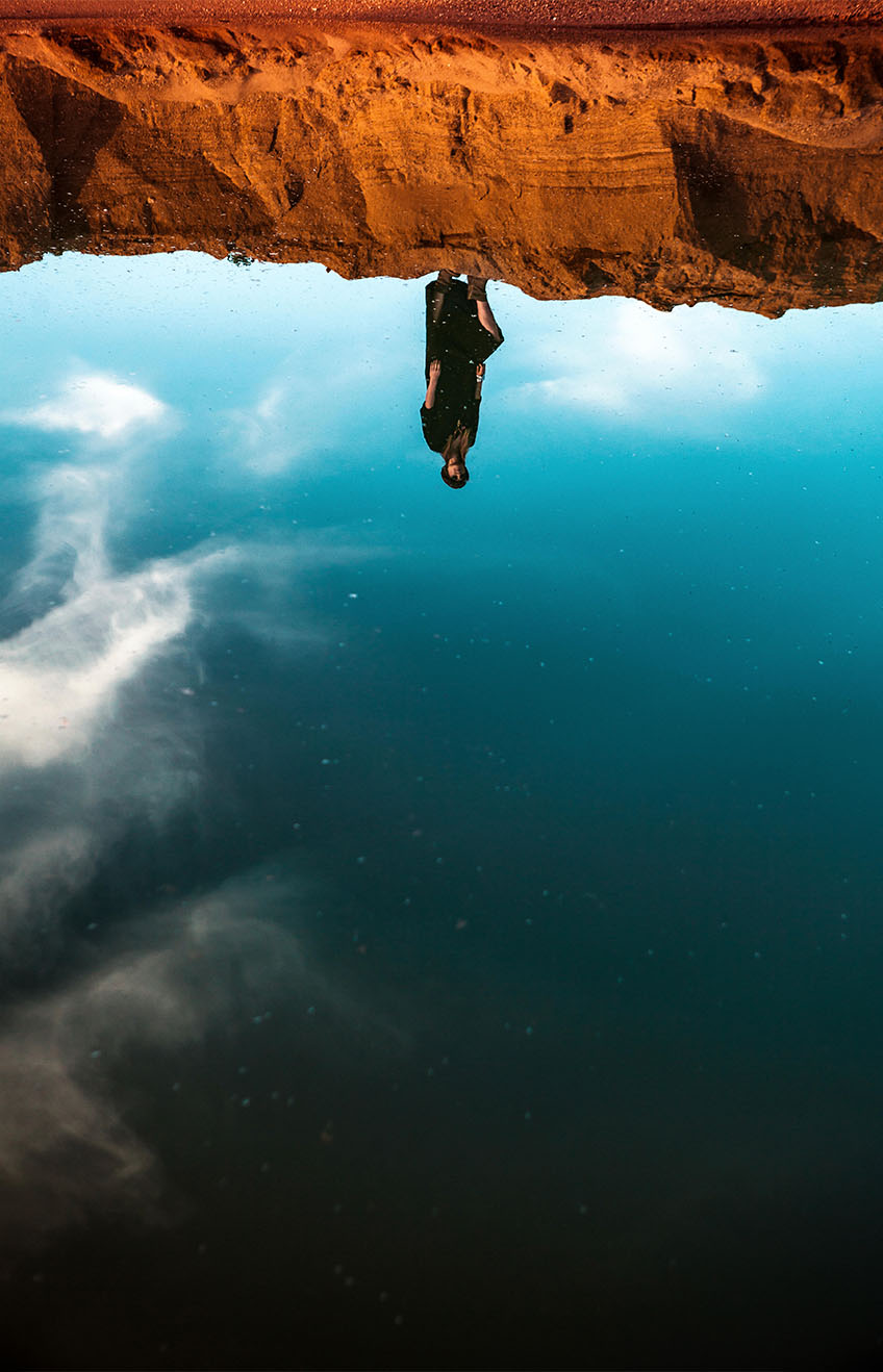 JB1PH9 - female standing on sand shore with reflection in water of her. oasis in desert